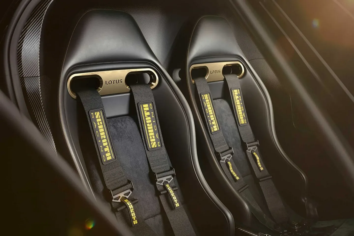 Rendering of the Lotus Type 62 interior: two black seats with gold harness plates and yellow Schroth racing harnesses.